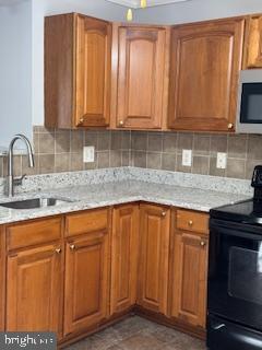 kitchen with tasteful backsplash, sink, light stone countertops, and black electric range