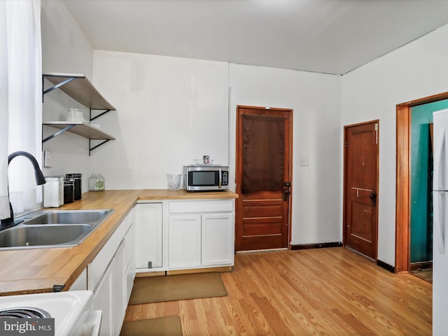 kitchen with sink, butcher block countertops, white cabinetry, stove, and light hardwood / wood-style floors