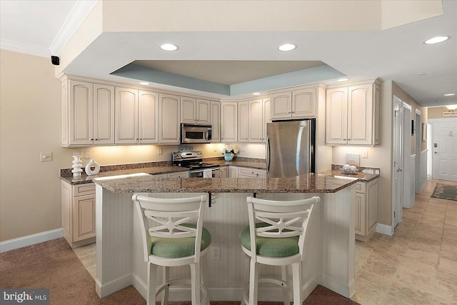 kitchen featuring dark stone countertops, stainless steel appliances, a breakfast bar, and a raised ceiling