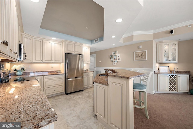 kitchen with a breakfast bar, a raised ceiling, a kitchen island, stone counters, and stainless steel appliances