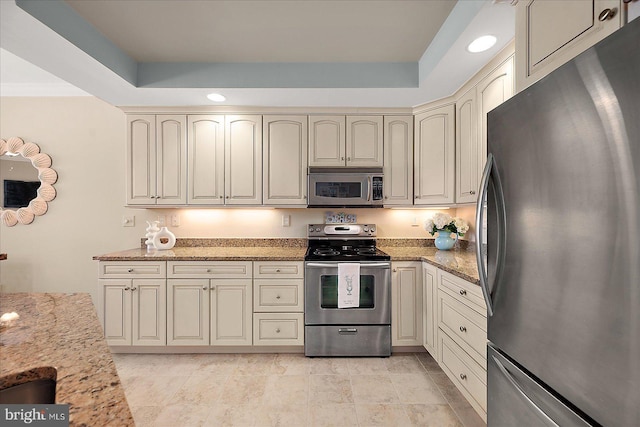 kitchen featuring a raised ceiling, light stone countertops, appliances with stainless steel finishes, and cream cabinetry