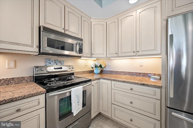 kitchen with stainless steel appliances, light stone countertops, light tile patterned floors, and cream cabinets