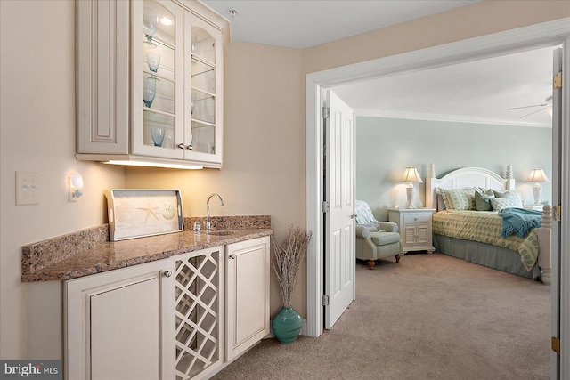 bar with sink, ceiling fan, stone counters, ornamental molding, and light colored carpet