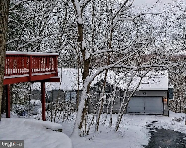 snow covered property with a wooden deck and a garage