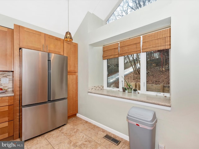 kitchen featuring backsplash, hanging light fixtures, vaulted ceiling, and stainless steel refrigerator