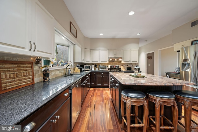 kitchen featuring a kitchen island, appliances with stainless steel finishes, white cabinets, dark brown cabinetry, and light stone countertops