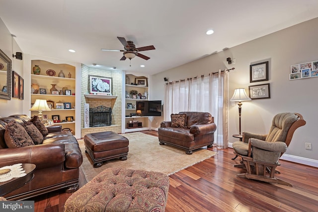 living room with built in shelves, ceiling fan, wood-type flooring, and a fireplace