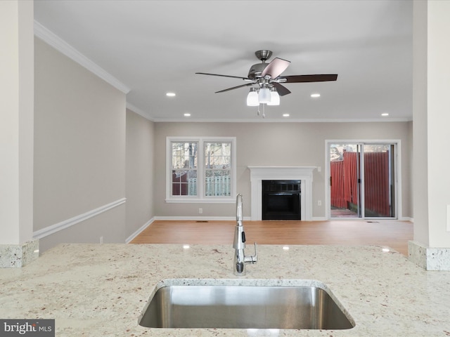 kitchen with sink, light hardwood / wood-style flooring, ornamental molding, ceiling fan, and light stone countertops