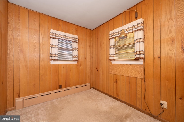 carpeted empty room featuring baseboard heating and wooden walls