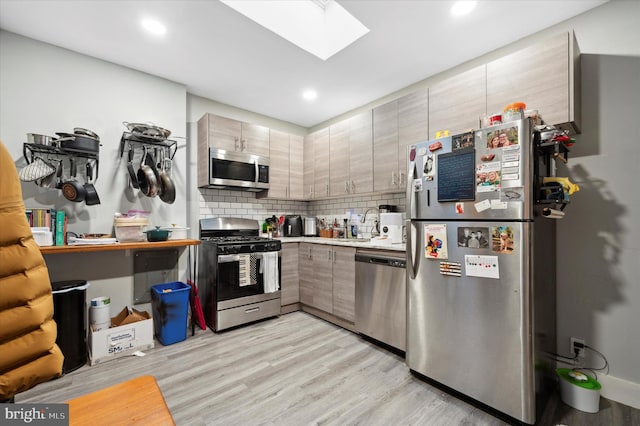 kitchen with light wood-type flooring, decorative backsplash, a skylight, and appliances with stainless steel finishes