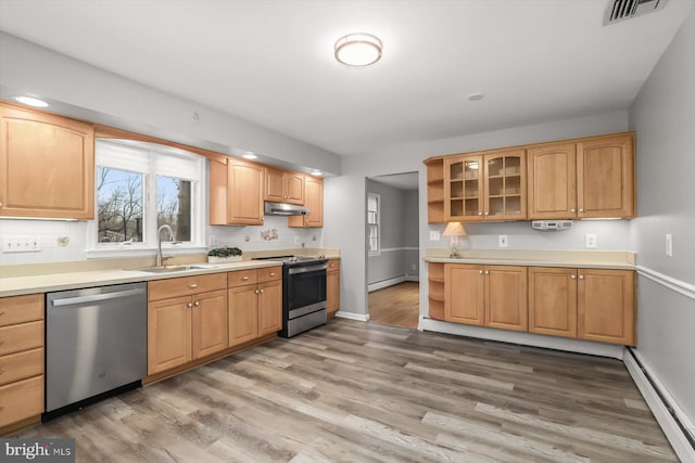 kitchen with stainless steel appliances, sink, baseboard heating, and light hardwood / wood-style flooring