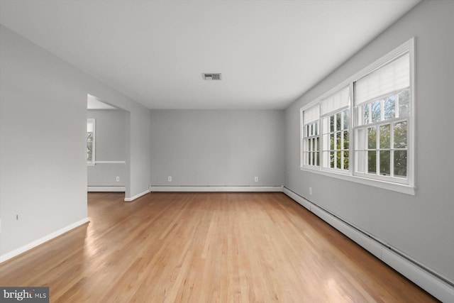 unfurnished room featuring a baseboard heating unit, light hardwood / wood-style flooring, and plenty of natural light