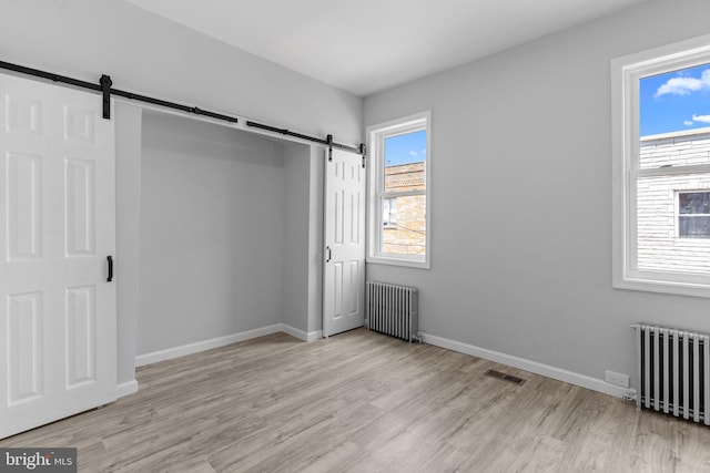 unfurnished bedroom featuring a barn door, radiator, and light hardwood / wood-style flooring