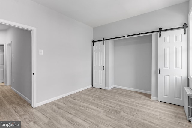 unfurnished bedroom with a barn door and light wood-type flooring