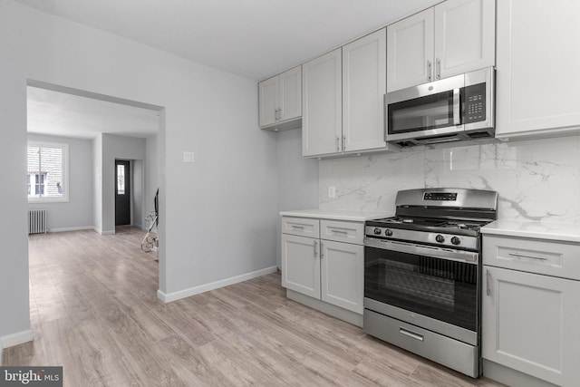 kitchen with stainless steel appliances, radiator, white cabinets, and decorative backsplash