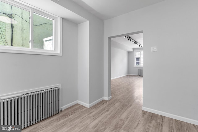 hallway featuring radiator heating unit, light hardwood / wood-style floors, and track lighting