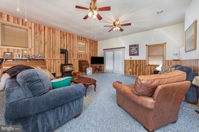 living room with ceiling fan, carpet flooring, a wood stove, and wood walls