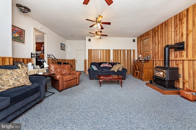 carpeted living room featuring a wood stove, ceiling fan, and wood walls