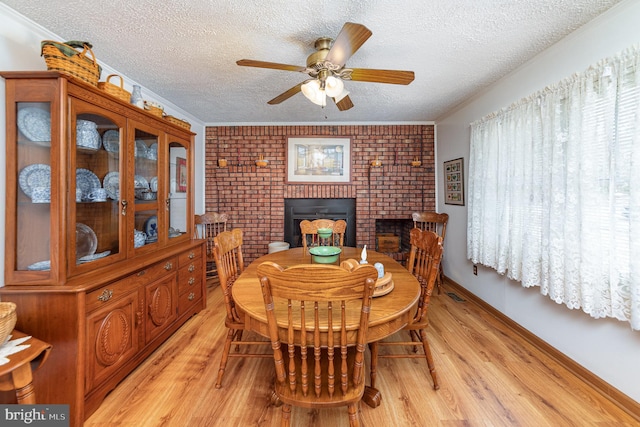 dining room with ornamental molding, a fireplace, a textured ceiling, and light hardwood / wood-style flooring