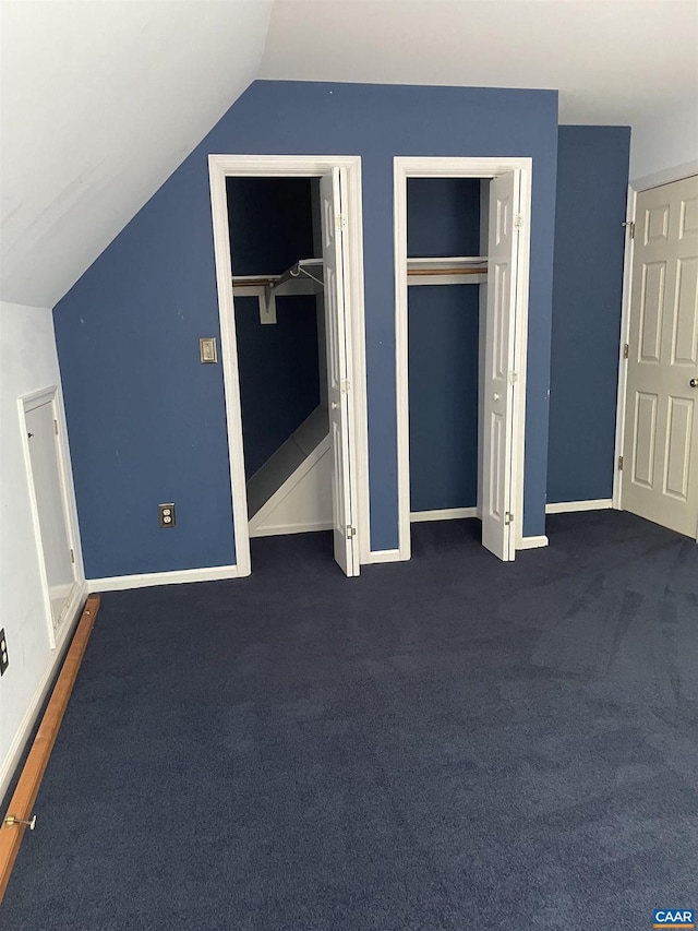 unfurnished bedroom featuring lofted ceiling, two closets, and dark carpet