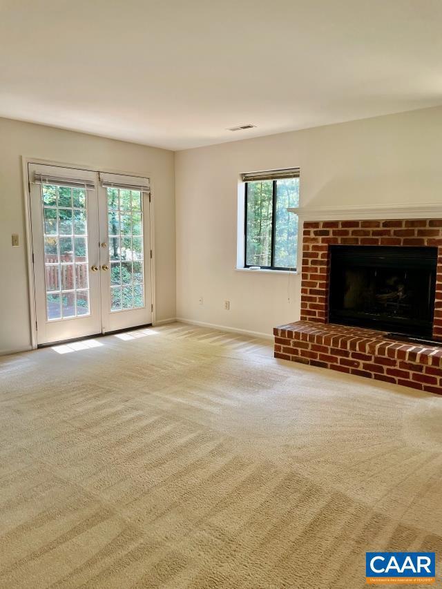 unfurnished living room featuring carpet floors, a fireplace, and french doors