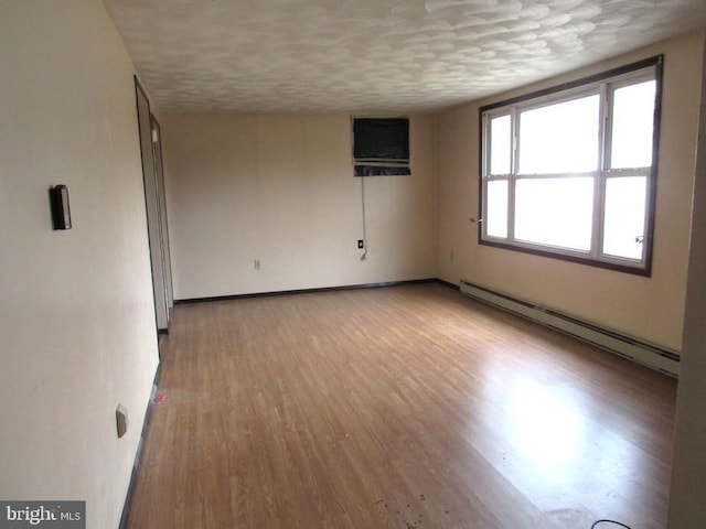 unfurnished room with an AC wall unit, light wood-type flooring, a textured ceiling, and baseboard heating