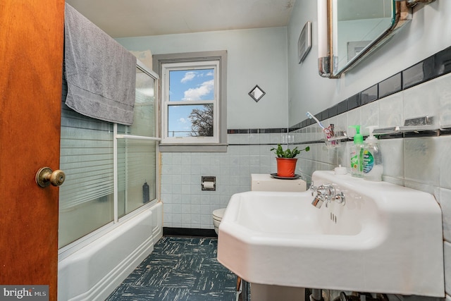 full bathroom featuring sink, tile walls, shower / bath combination with glass door, and toilet