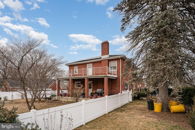 back of property featuring a lawn, a balcony, and solar panels