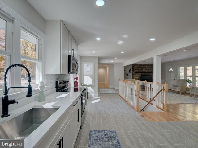 kitchen with a fireplace, tasteful backsplash, white cabinetry, sink, and stainless steel appliances