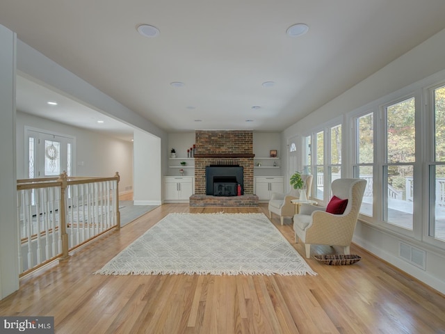 living room featuring light wood-type flooring, a brick fireplace, and a wealth of natural light