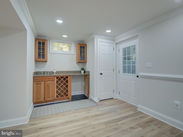 bar with light stone counters, ornamental molding, sink, and light hardwood / wood-style floors