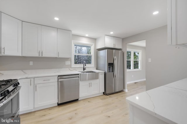 kitchen featuring sink, white cabinetry, light stone counters, stainless steel appliances, and light hardwood / wood-style floors