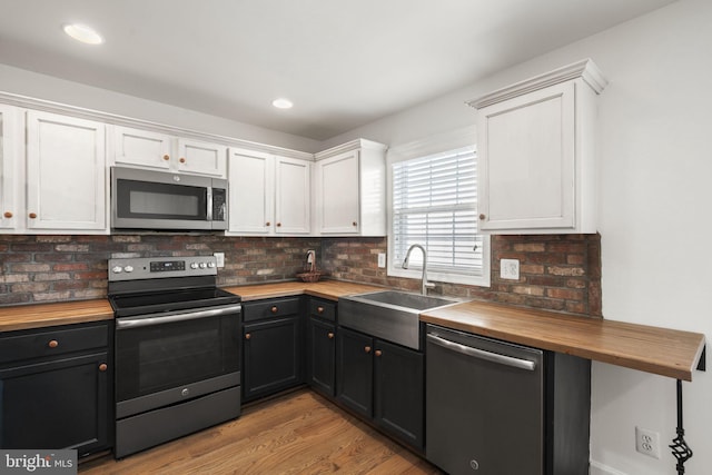 kitchen with butcher block countertops, stainless steel appliances, sink, and white cabinets