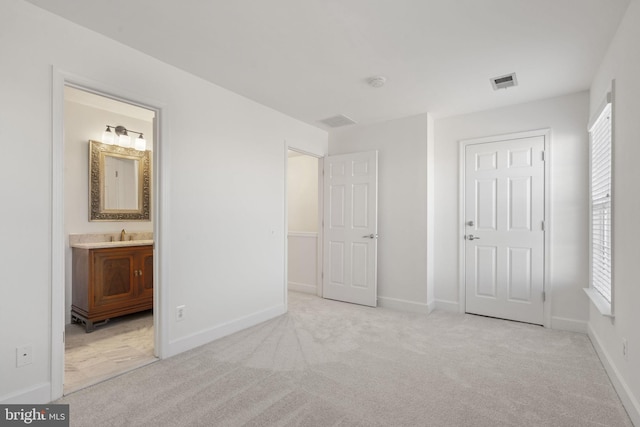 unfurnished bedroom with multiple windows, ensuite bath, and light colored carpet