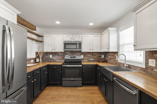 kitchen with white cabinetry, sink, stainless steel appliances, and butcher block countertops