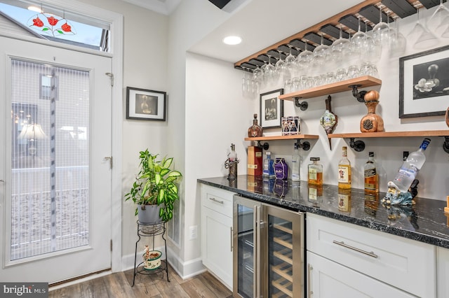 bar with dark stone countertops, beverage cooler, wood-type flooring, and white cabinets