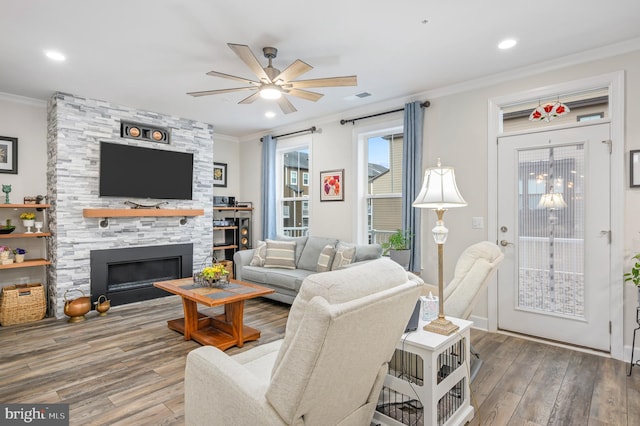 living room featuring ceiling fan, ornamental molding, a stone fireplace, and wood-type flooring