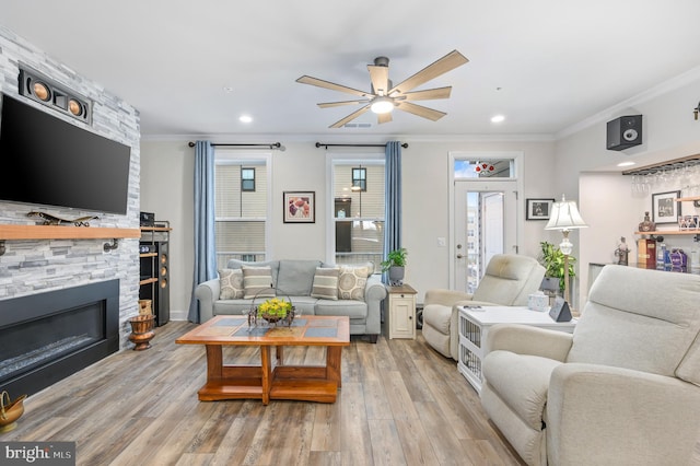 living room featuring crown molding, light hardwood / wood-style flooring, a stone fireplace, and ceiling fan