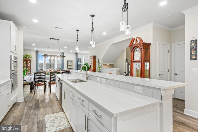 kitchen featuring stainless steel appliances, a sink, light wood-style floors, a large island with sink, and crown molding