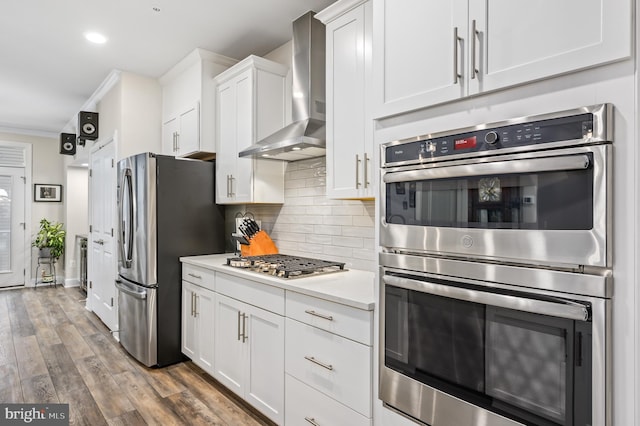 kitchen with tasteful backsplash, wall chimney range hood, dark hardwood / wood-style flooring, stainless steel appliances, and white cabinets