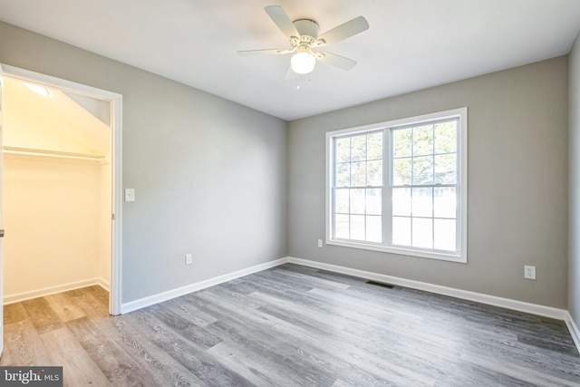 unfurnished bedroom featuring ceiling fan, a walk in closet, a closet, and light wood-type flooring