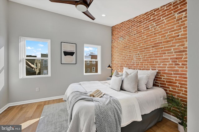 bedroom featuring ceiling fan, brick wall, and light hardwood / wood-style flooring