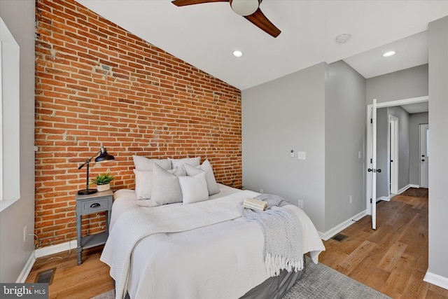 bedroom featuring lofted ceiling, light hardwood / wood-style floors, ceiling fan, and brick wall