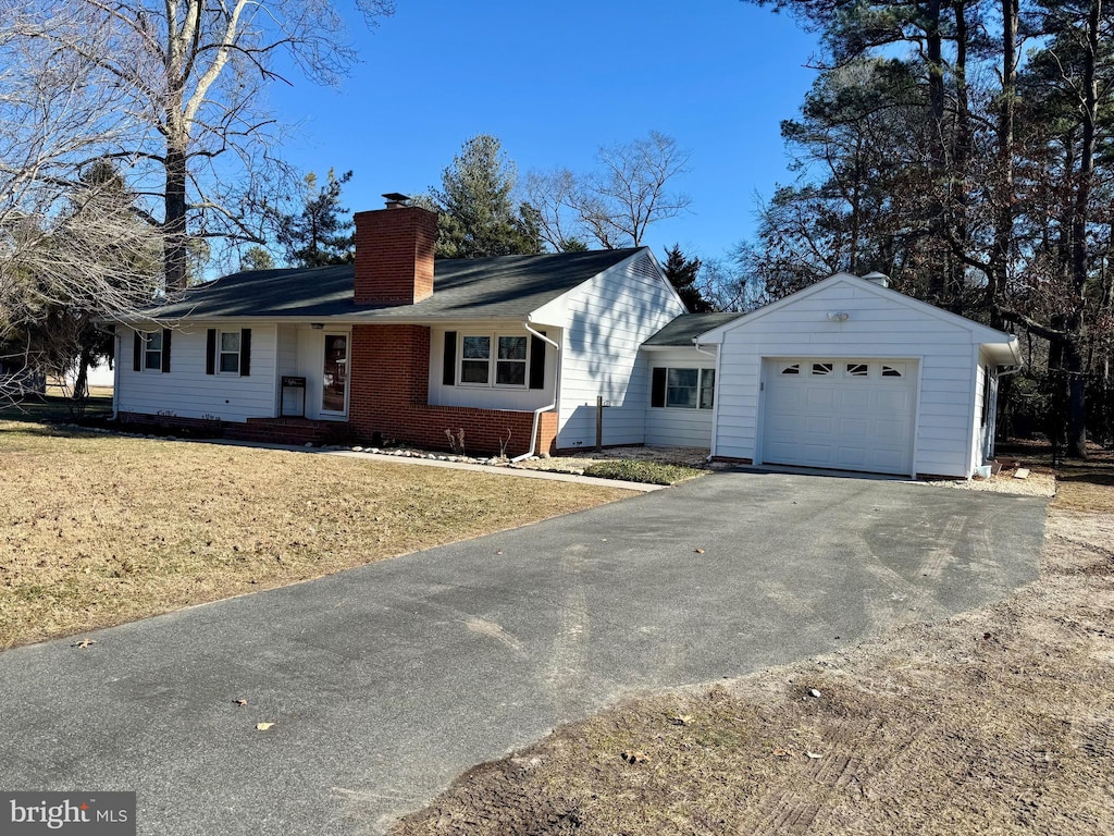 ranch-style house with brick siding, a chimney, a garage, driveway, and a front lawn