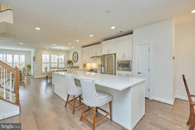 kitchen featuring a breakfast bar area, white cabinetry, light hardwood / wood-style flooring, appliances with stainless steel finishes, and a large island