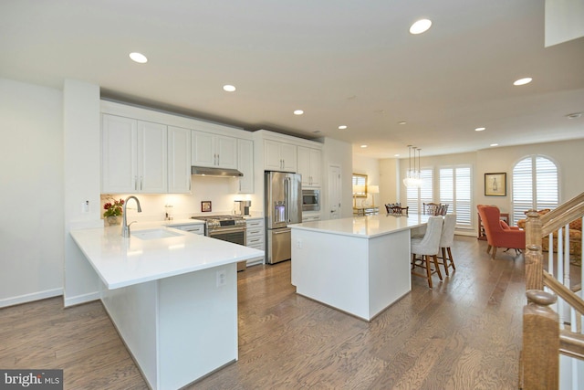 kitchen with a kitchen bar, sink, high quality appliances, kitchen peninsula, and pendant lighting