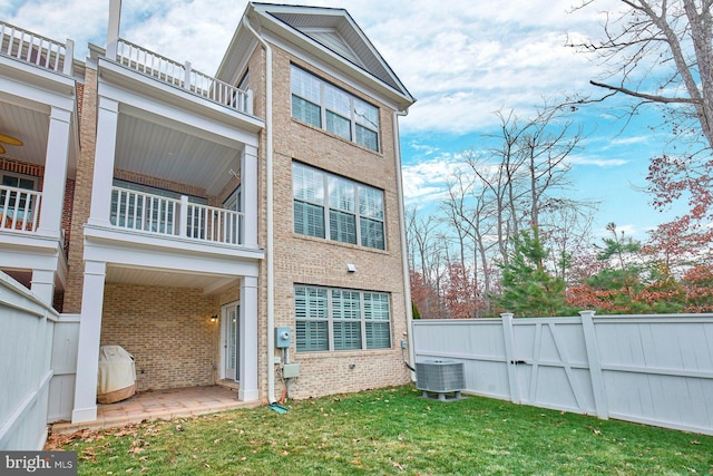 back of house featuring a balcony, a patio, central AC unit, and a lawn