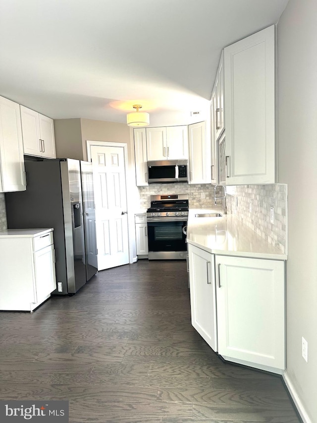 kitchen featuring appliances with stainless steel finishes, white cabinetry, sink, backsplash, and dark wood-type flooring