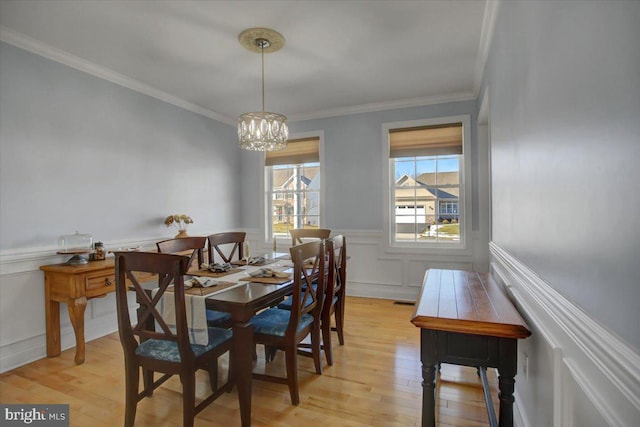 dining area with ornamental molding, a notable chandelier, and light hardwood / wood-style flooring