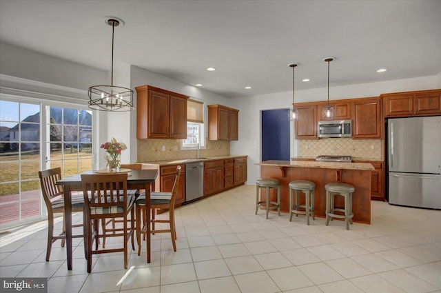 kitchen with pendant lighting, sink, stainless steel appliances, a center island, and light stone countertops